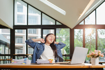 Smiling young Asian woman clearing paperwork in office, using laptop and many documents beside her. Accounting and finance business concept.