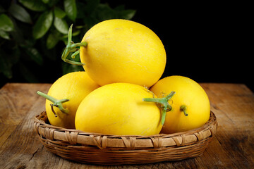Sweet Yellow Honeydew Melons in Wicker Basket on Rustic Wood Table with Green Leaves Background