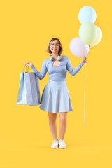 Beautiful woman with shopping bags and balloons on yellow background