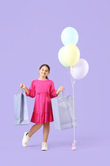 Little girl with gift bags and balloons on lilac background