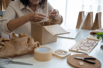 Mature asian woman business E-commerce entrepreneurship owner preparing Packing packages In Cardboard Box to ship to customers.