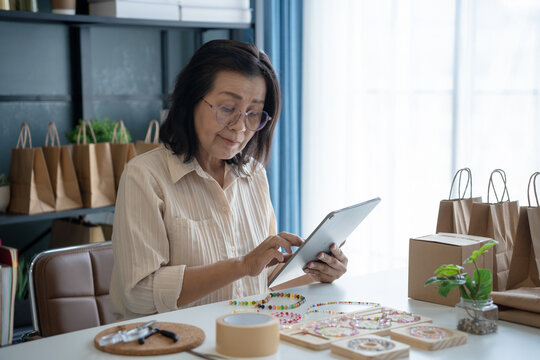 Mature asian woman business owner E-commerce online orders with tablet entrepreneurship jewellery accessories handcraft Cardboard Box.