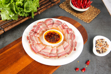 Smoked pork belly slices on wooden plate with spicy sauce and fresh vegetables