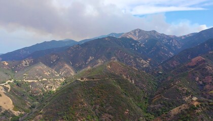 Obraz premium Scenic aerial view of a mountain range with lush green vegetation and cloudy skies
