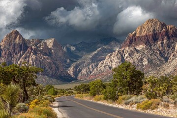 A desert road winds through a valley, leading towards dramatic, storm-lit mountains