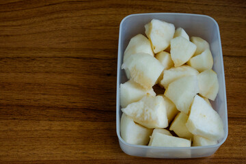 A clean, top-down shot of a white container filled with sliced pears, ready to eat. The container is placed on a simple wooden table, perfect for themes of healthy snacks, fresh fruit, healthy eating.