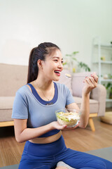 Asian adult woman eats healthy meal bowl breakfast home fitness active lifestyle wellness nutrition post workout recovery energy indoor living room