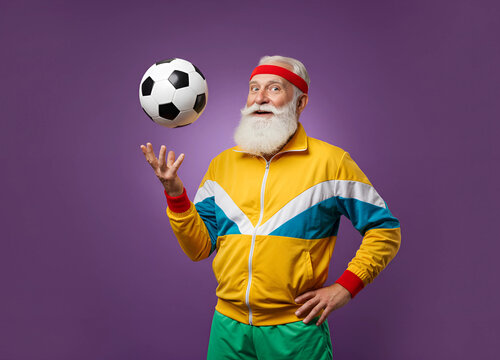 Joyful senior man in retro tracksuit juggles soccer ball with a smile, radiating fun and vitality.