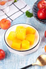 Fresh Yellow Peach Cubes in Syrup with Red Plums and Seasonal Fruits on Blue Wooden Table
