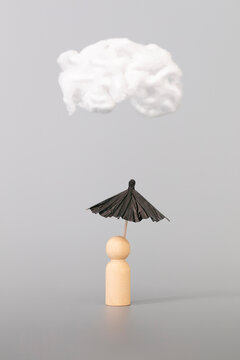 Psychology, solitude, fear or mental health problem concept. Depressed sad person with a cloud overhead, on grey background. Wooden figure with black umbrella symbolize mental health. Vertical format.