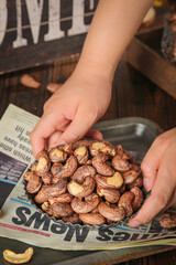 Hands Holding Fresh Roasted Cashew Nuts on Newspaper - Healthy Snack Food Preparation