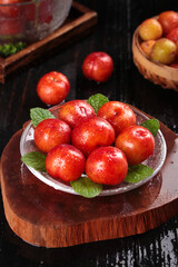 Fresh Red Guangdong Plums with Mint Leaves on Wooden Board - Crisp Sour Asian Fruits Display