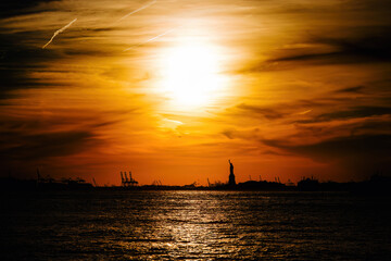 The silhouette of the Statue of Liberty in New York in with a dramatic sunset sky