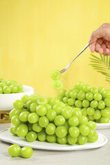 Fresh Green Grapes on Plate with Fork Against Sunny Yellow Background - Healthy Fruit Eating Concept