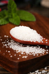 White Granulated Cane Sugar in Wooden Spoon with Fresh Mint Leaves on Rustic Kitchen Counter