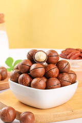 Top view macadamia nuts in bowl with cream colored kernels, flavored nut arrangement on wooden cutting board