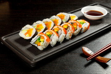 Japanese Sushi Rolls with Seaweed Wrapped Rice on Black Platter Display with Soy Sauce and Chopsticks
