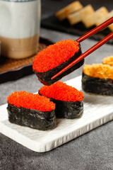 Japanese tobiko roe sushi with chopsticks on marble platter - traditional seaweed wrapped delicate dish