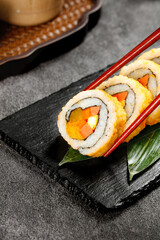 Fresh Sushi Rolls with Salmon and Vegetables on Black Slate with Red Chopsticks and Traditional Tea Setting