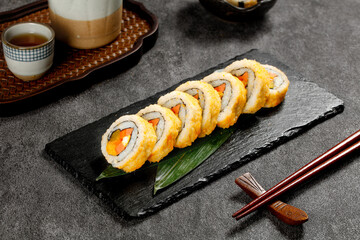 Japanese Sushi Rolls with Salmon and Egg on Slate Plate with Tea Service and Chopsticks