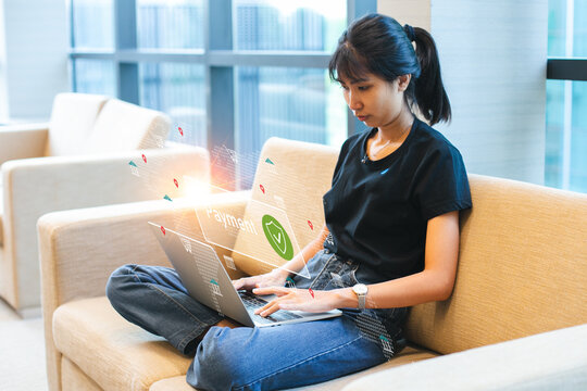 Asian woman using laptop with digital payment interface overlay, representing online transaction, fintech, secure payment system, and e-commerce technology.
