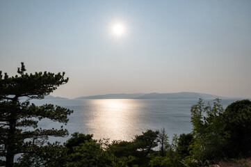 Sun over the sea, an island in the background and trees in the foreground