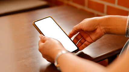 In a warm, inviting indoor space, an individual is holding a smartphone with a blank screen. The wooden table reflects a relaxed atmosphere, ideal for communication or browsing