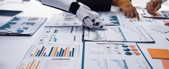 A robotic arm collaborates with a team of professionals in an office setting, analyzing data through various charts and graphs displayed on the table.Noogenesis