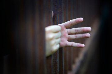 Hand Reaching Through Rusty Bars Representing Despair and Isolation