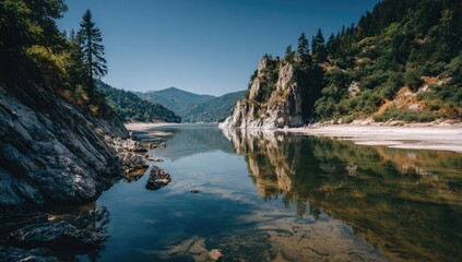 Obraz premium Calm lake reflecting mountains and trees under a clear blue sky