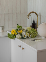 A bouquet of autumn flowers of hydrangeas, dahlias, in the sink, ceramic vase, pruner in the kitchen. Flower care concept
