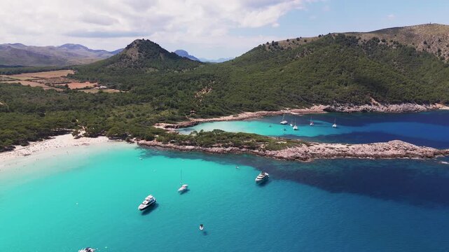 Aerial Drone Panning Shot Over Anchored Boats In Cala Agulla Bay Towards Pine Forest Mountains, Mallorca, Spain