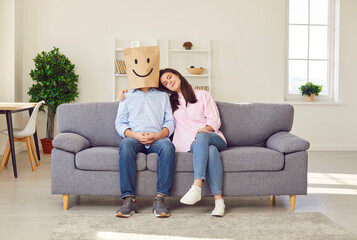 A paper bag with a smile drawn on a man's head, a woman hugging him. A married couple is sitting on the couch at home, hugging each other. Pretense in marriage, reconciliation in relationships