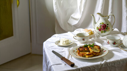  An elegant still life featuring a delicious brunch with French toast or pastries, accompanied by a beautiful vintage floral tea set on a pristine white tablecloth. Soft natural light illuminates the 