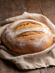 A loaf of sourdough bread resting on a beige linen cloth placed on a rustic wooden table surface top view