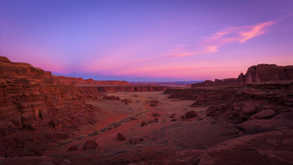 Naklejka premium A scenic canyon landscape during sunset with a vibrant purple and pink sky above the rock formations