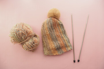 Knitted beanie with pom pom and knitting supplies on table