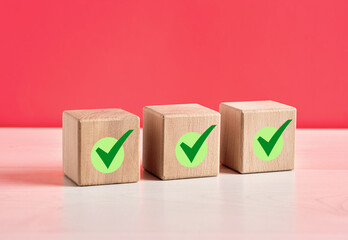 Three Wooden Cubes Showing Check Marks Symbolizing Validation on Pink Background