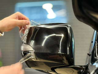 Car wrapping, detailing, tuning and styling. PPF protective film against chips and scratches. Car protection. A car wrapping specialist applies a polyurethane film on the car side mirror close-up. 