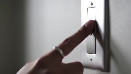 Finger flicks a light switch on a white wall, illuminating the room with a soft glow, symbolizing energy use and home automation. - Powered by Adobe