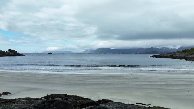 Rorvik Beach in spring with freezing Arctic water and photographer&rsquo;s camera placed on rock by shore, rising aerial.