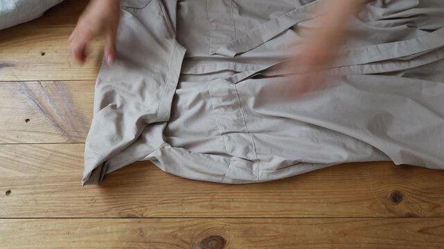 A person demonstrates a simple method for folding sheets neatly on a wooden floor, emphasizing organization and practicality in home management