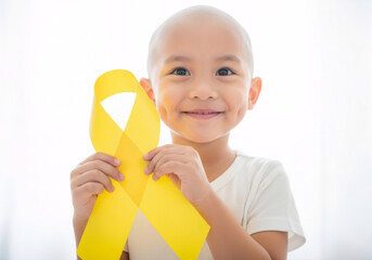 Bald little asian kid holding yellow ribbon on white background. Cancer awareness symbol. Childhood cancer awareness month. Hospital support close up concept.