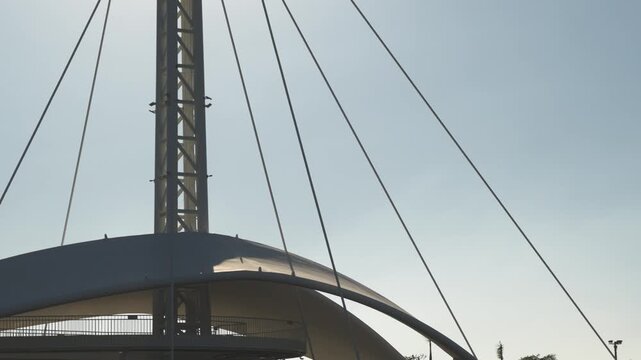 Modern architectural detail with sunlit mast and wires against clear sky backgro