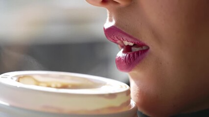 Woman drinking coffee from paper cup in bright cafe, enjoying the warm beverage on a chilly morning, creating a cozy and comforting atmosphere.