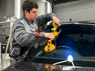 Automobile special workers replacing windscreen or windshield of a car in auto service station...