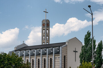 Obraz premium Catholic Cathedral of St. Joseph Parish with modern architectural design, featuring its clock tower, cross, and facade details under a bright summer sky.