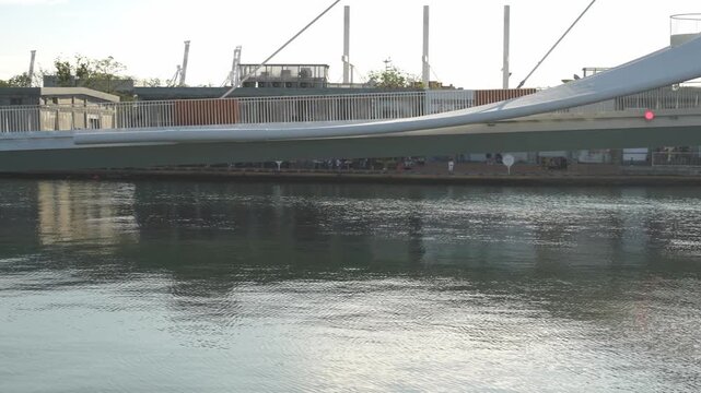 Modern pedestrian bridge over tranquil river with industrial background at sunse