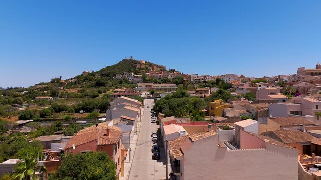 Aerial Drone Shot Low Altitude Approach Over Capdepera Town Rooftops Towards Historic Castell de Capdepera, Mallorca, Spain, on a Bright Summer Day.