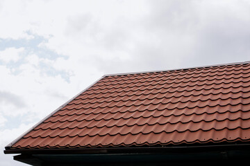Red metal tile roof of a house against a cloudy sky, close-up view of clean roofing surface with copy space